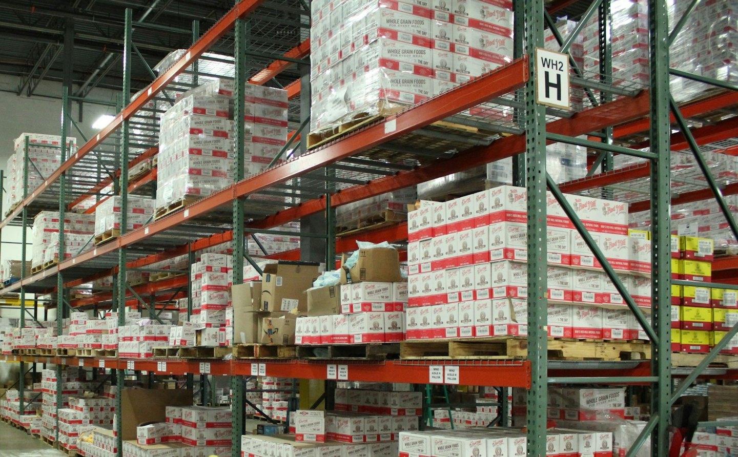 Rijen hoge metalen stellingen vol met dozen in een magazijn.
